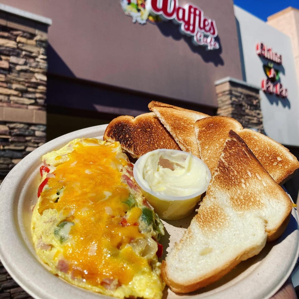 A cheesy omelet with toast and butter on a plate, with the Waffles Café sign in the background.