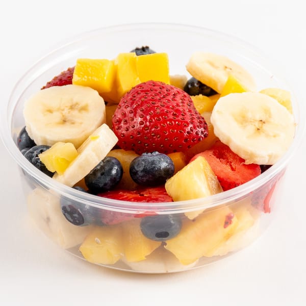 A clear plastic container filled with fresh fruit salad, including strawberries, blueberries, bananas, and mango.