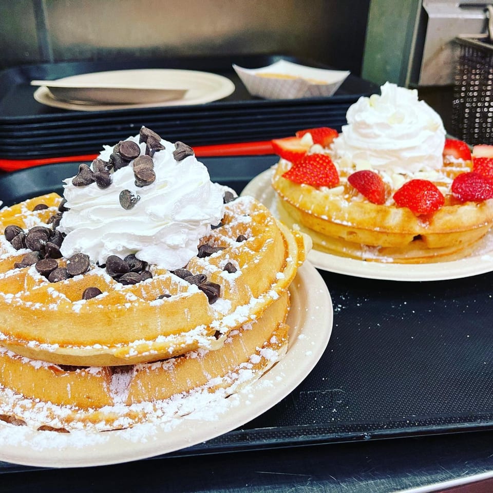 Two Waffles Café waffles, one with chocolate chips and the other with strawberries and whipped cream.