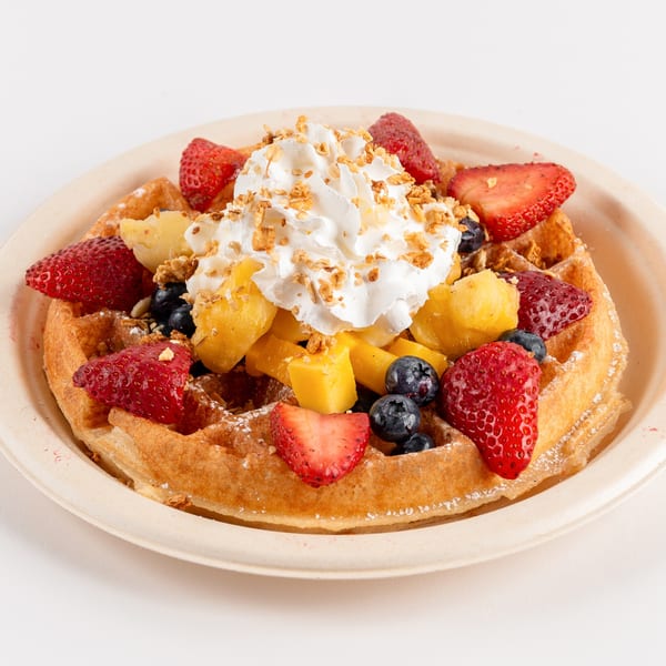 Golden Waffles Café waffle topped with whipped cream, strawberries, blueberries, and mango on a plate.
