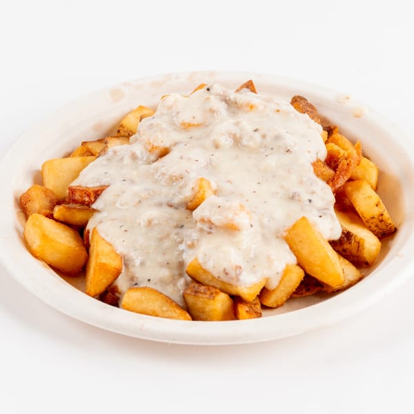 Golden-brown home fries covered in creamy white sausage gravy, served in a light-colored bowl.